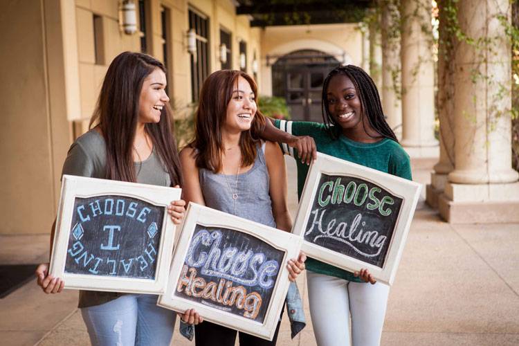 Three female CBU students holding chalkboards with messages about healing